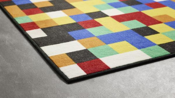 „Farbenfroher Vorwerk Teppich mit pixelartähnlichem Quadratmuster in Rot, Blau, Gelb, Grün, Schwarz und Weiß auf grauem Boden; umlaufend dunkel gekettelt.“